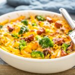 A bowl of mac and cheese topped with bacon and broccoli.