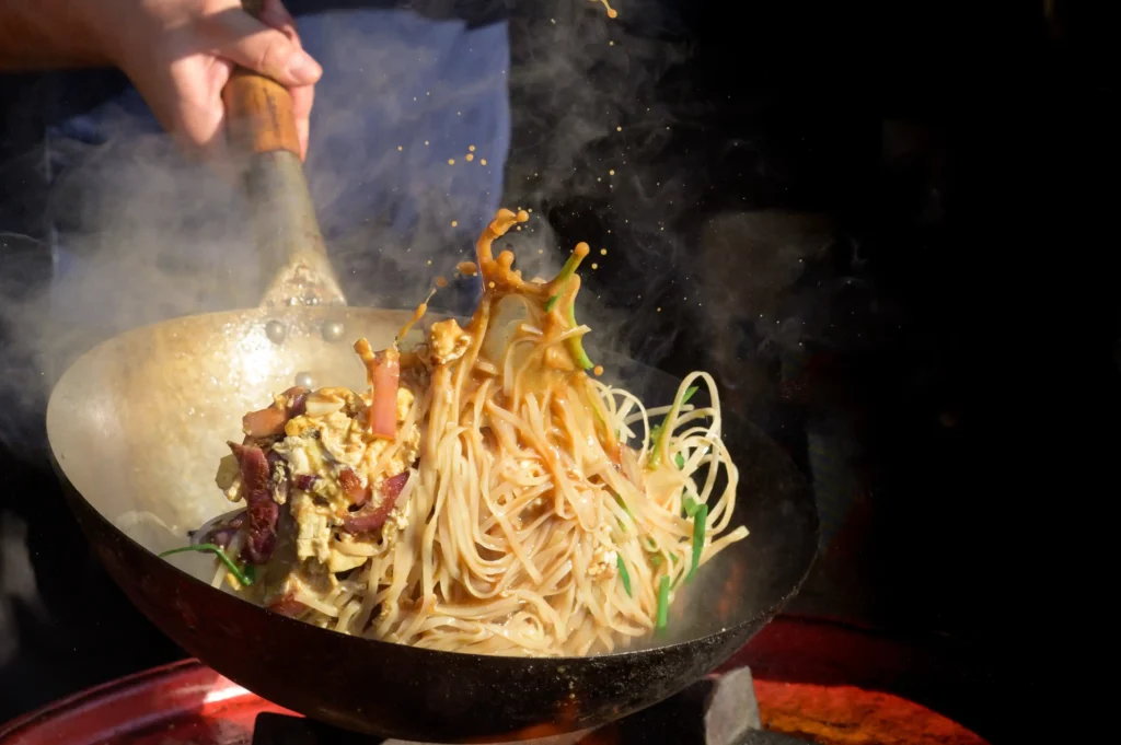 Rice noodles soaking in warm water and being rinsed under cold water.