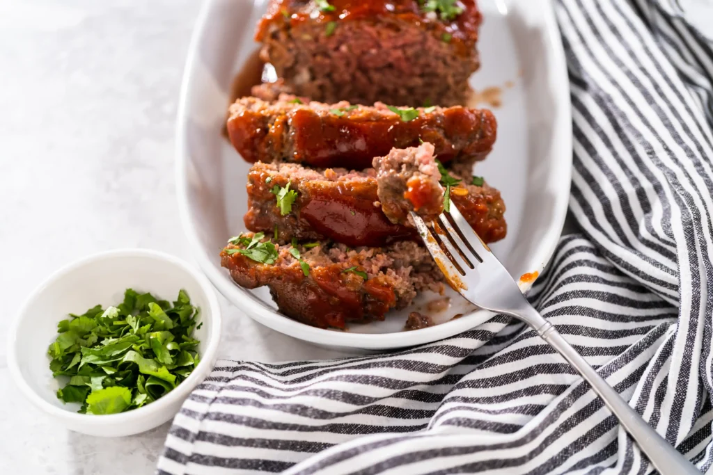 A perfectly baked meatloaf glazed with ketchup and garnished with parsley ready to eat.