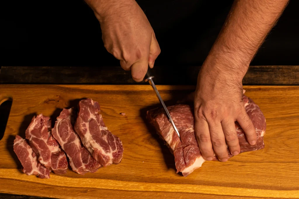 Raw brisket being trimmed on a cutting board.