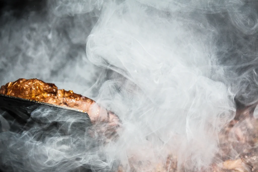 A smoker filled with wood chips, with smoke rising