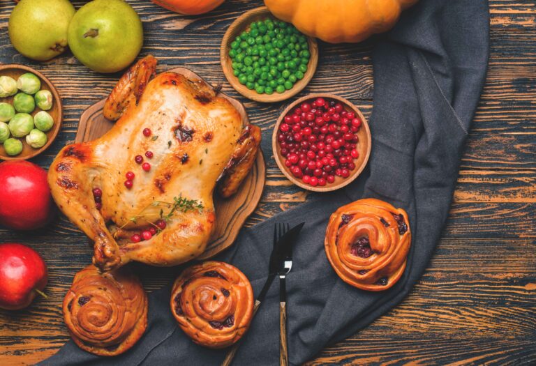 Freshly roasted rotisserie chicken on a wooden cutting board with fresh herbs and spices around