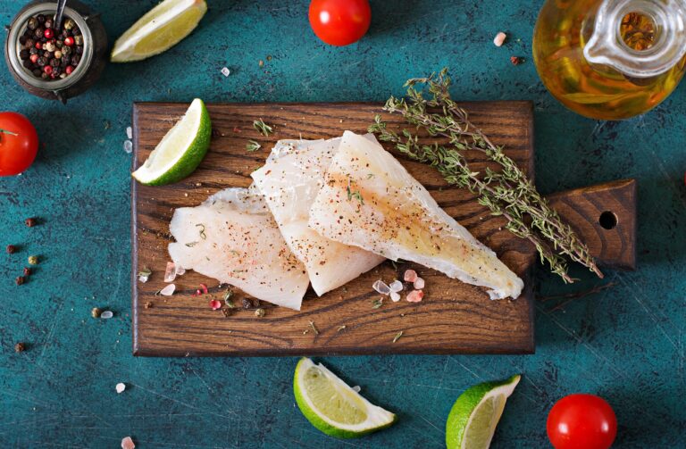 Rockfish fillets on a cutting board with lemon wedges and herbs.