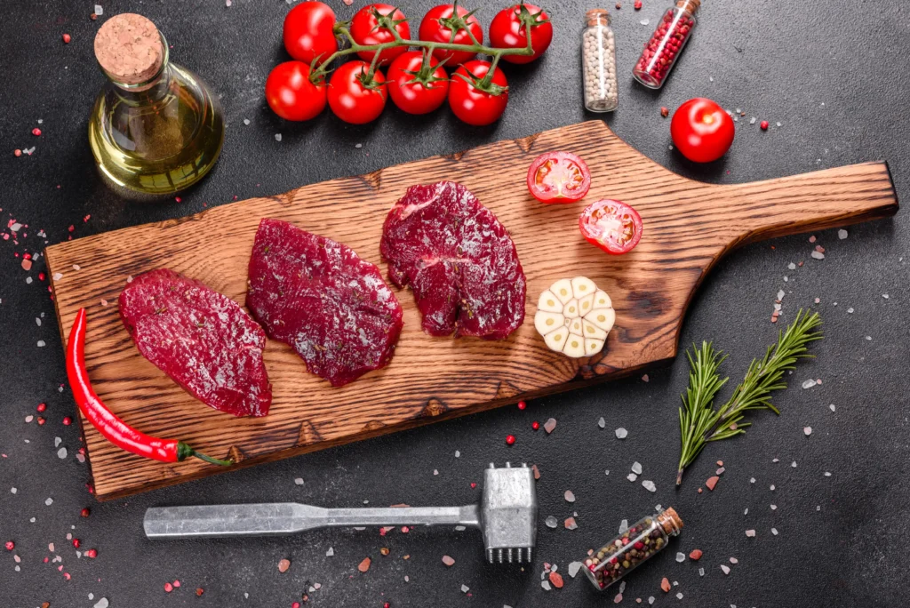 Fresh bison meat on a cutting board with spices and vegetables nearby