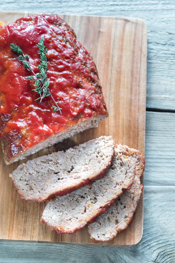 A perfectly sliced smoked meatloaf on a wooden cutting board with grill marks, garnished with parsley and served with mashed potatoes.