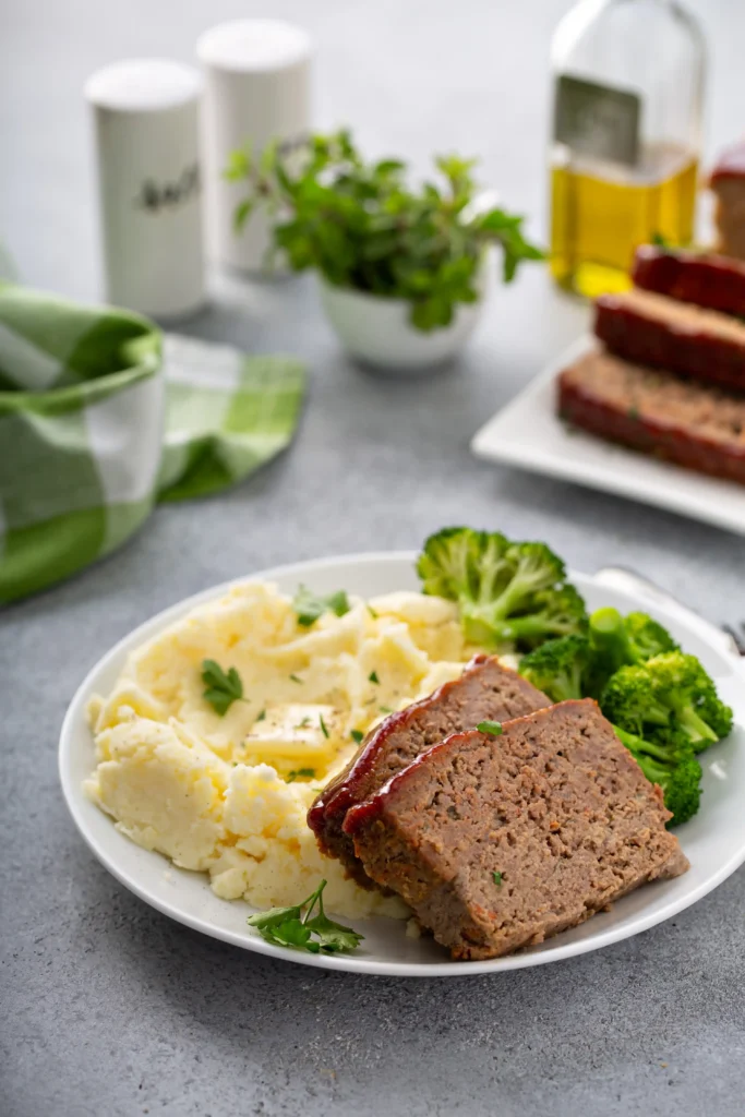 A sliced smoked meatloaf served with mashed potatoes and green beans