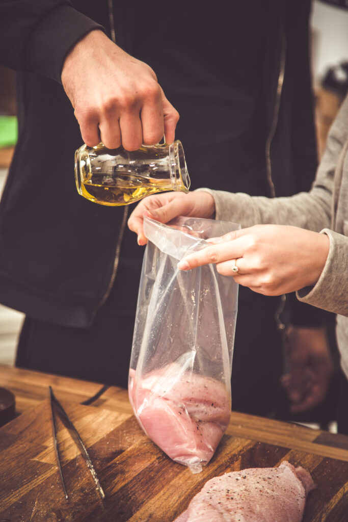  A chef pounding chicken breasts with a meat mallet inside a ziplock bag.