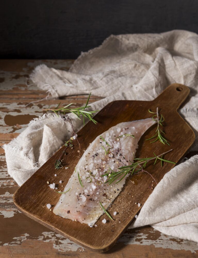 Fresh rockfish fillets with herbs and lemon on a wooden cutting board.