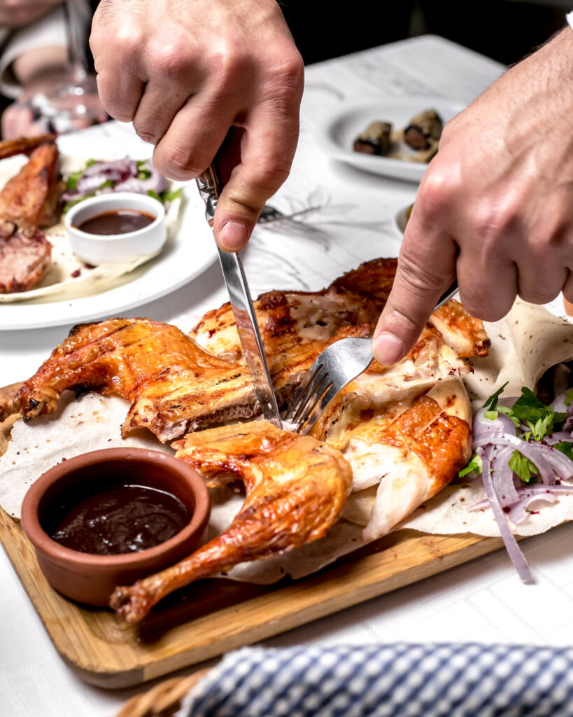 Hands carving a rotisserie chicken on a cutting board