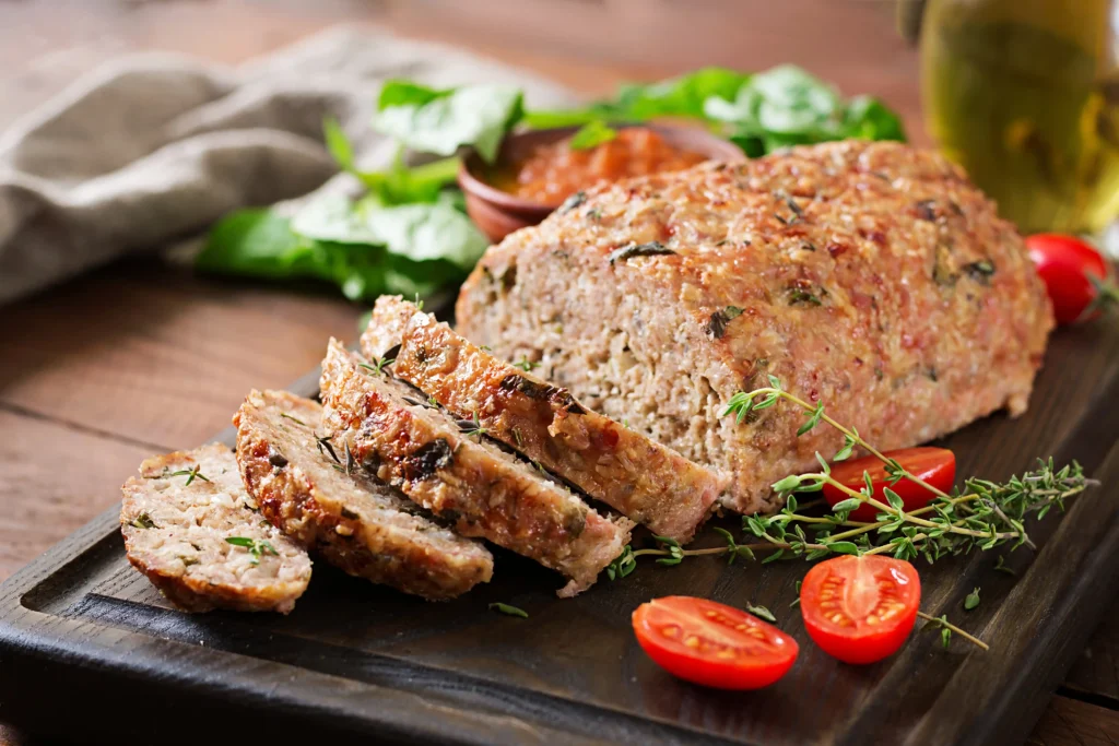 A freshly baked Italian meatloaf garnished with fresh parsley and served with marinara sauce on a wooden platter.