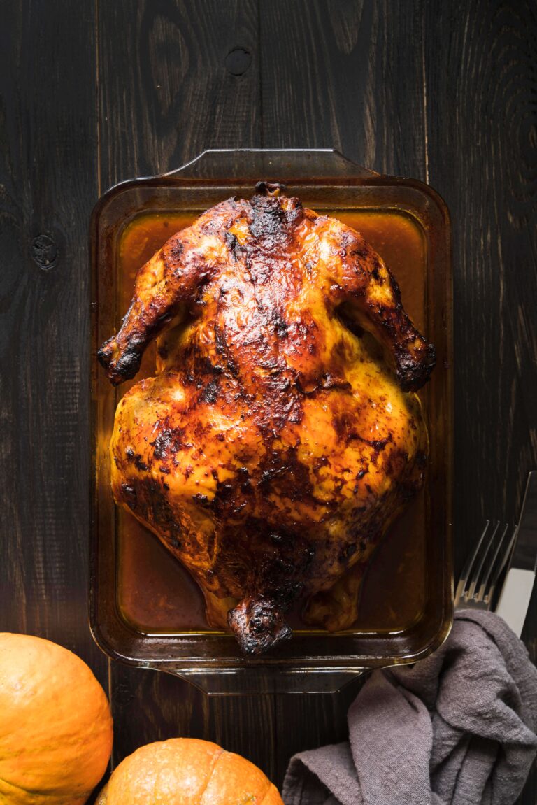 Rotisserie chicken on a cutting board surrounded by fresh vegetables and seasonings