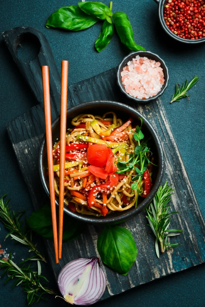 A colorful bowl of Thai noodles garnished with fresh herbs, lime, and peanuts.